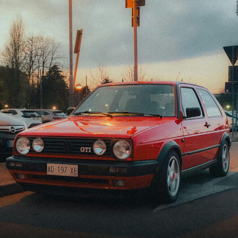 Vintage red Volkswagen GTI parked outdoors at sunset creating a vibrant classic car scene.
